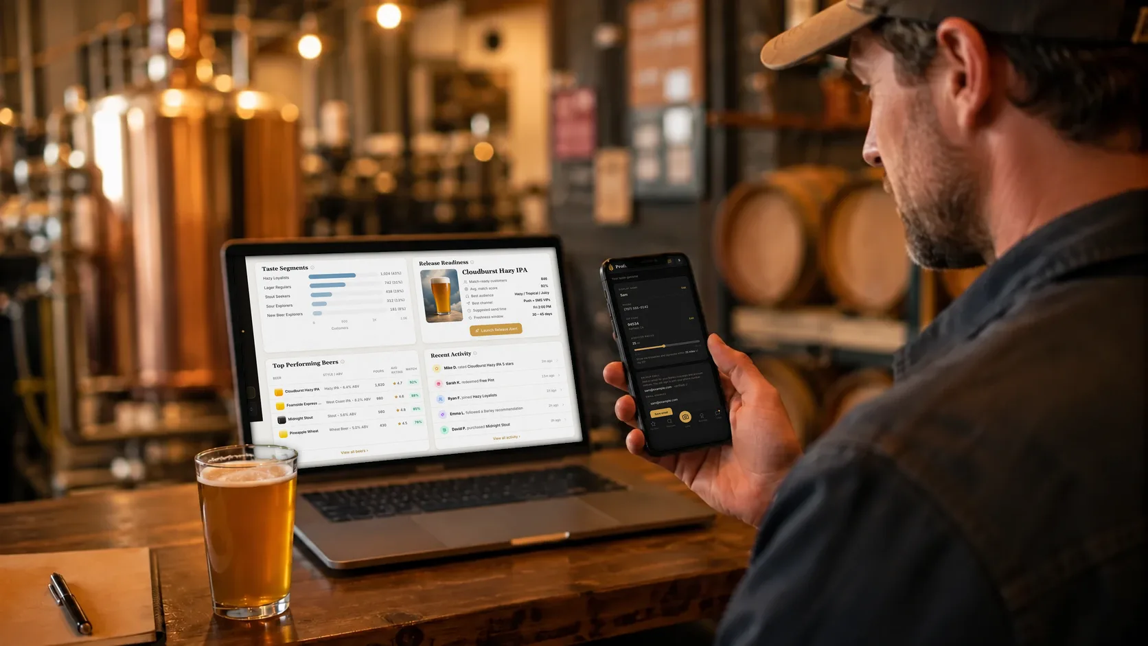 A brewer holds a phone open to the Barley app's profile screen beside a laptop showing the Brewlytics Overview at the release readiness card for Cloudburst Hazy IPA.