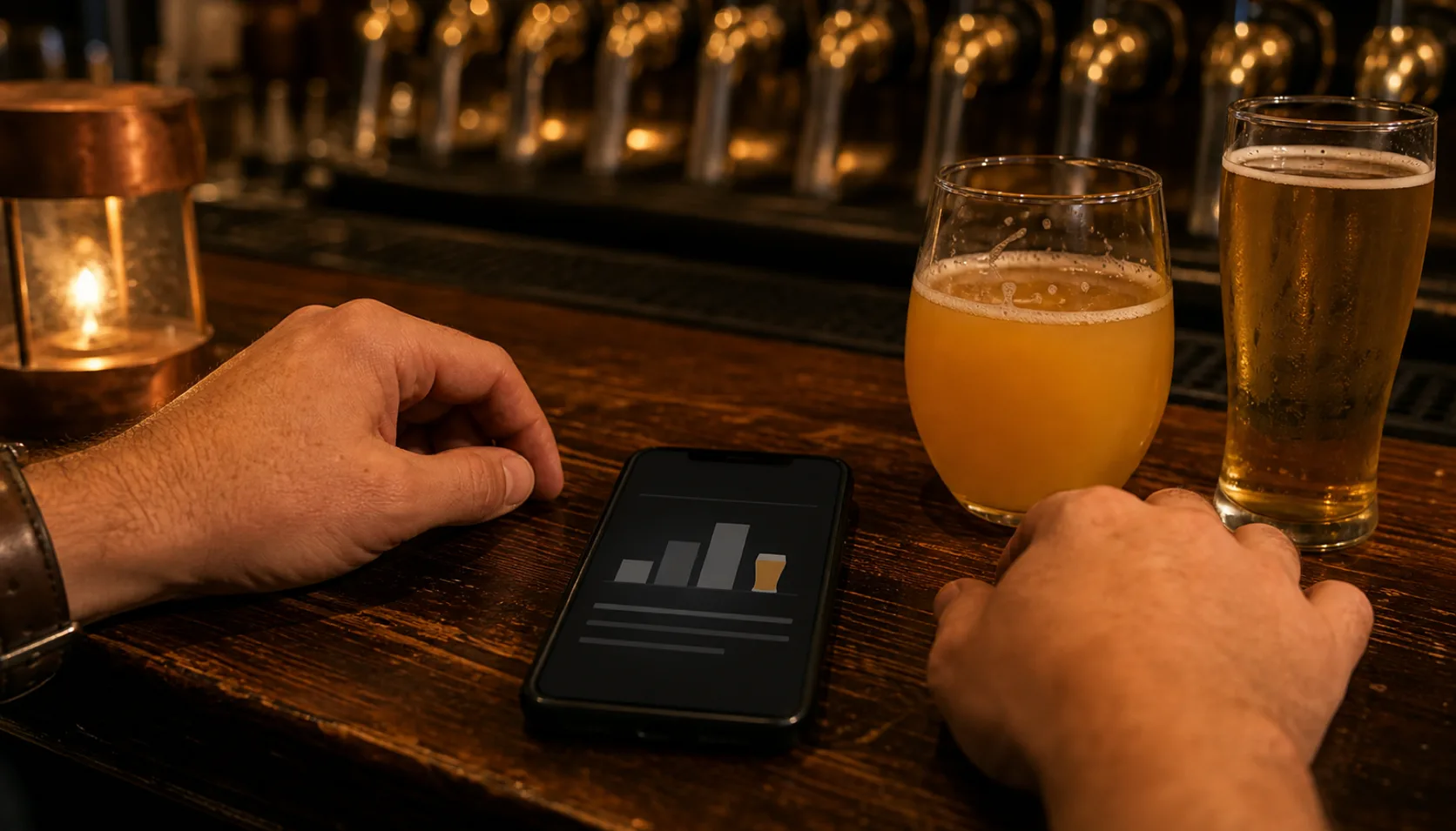 A phone lies face up on a bar between two hands and two glasses of beer, its screen showing a simple bar chart card, with a row of brass tap handles out of focus behind.