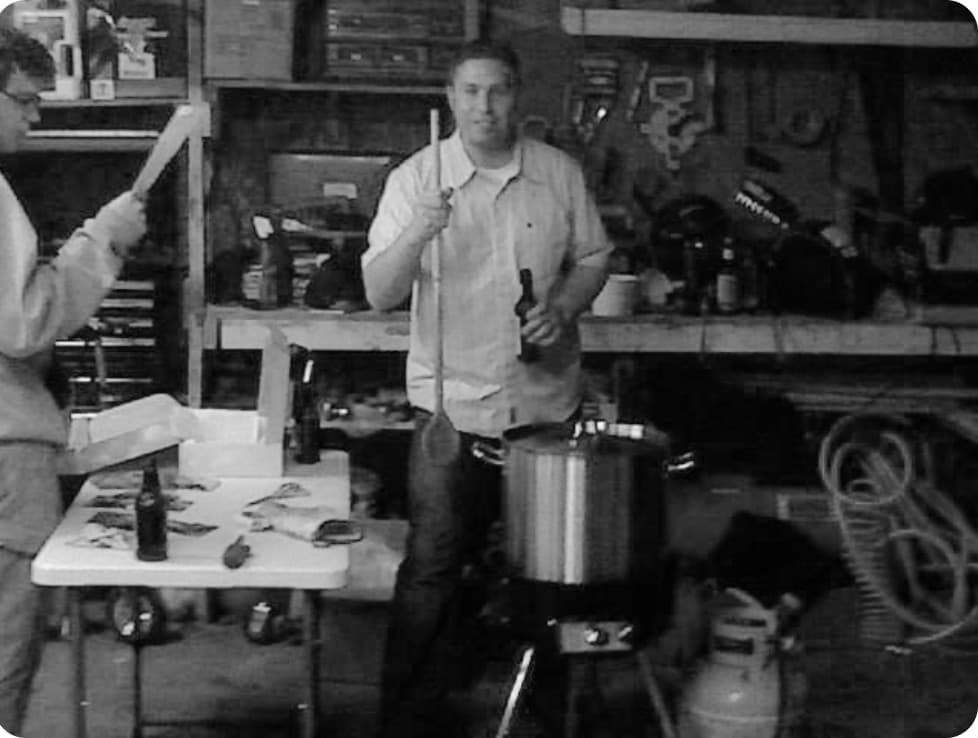 Brian Winckel brewing his first batch of beer in a garage in 2008, stirring a kettle over a propane burner